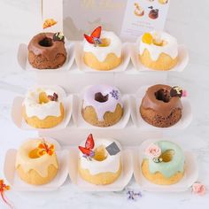 there are many different donuts in the trays on this counter top, and one is decorated with icing