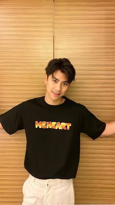 a young man standing in front of a wooden wall