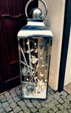 a lantern with branches and flowers in it sitting on the ground next to a building