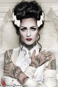 a woman with black hair and tattoos on her face, wearing white gloves and holding hands in front of her chest