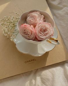 pink roses in a white bowl with gold handles on top of a table cloth covered placemat