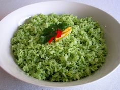 a white bowl filled with green rice and a small red object in the middle of it