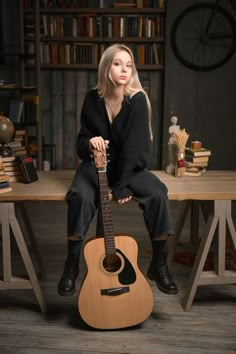 a woman sitting on top of a wooden table with a guitar in front of her