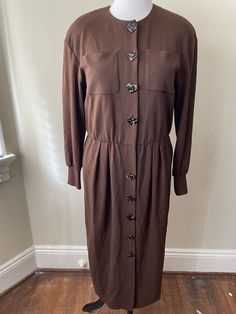 "Vintage brown button up dress. Rayon blend with nylon and lycra, feels like sweatshirt material. Long sleeve, heart tortiseshell button up front, pockets. Dry clean only.  Please ask questions!  Measurements (laid flat):  Tag Size: 14 Length: 49\" Pit to Pit: 21\"x2 Waist: 17\"x2 Hips: 21\"x2 Condition: Excellent vintage condition, no issues noted.  The vintage pieces I sell have all led a previous life and may tell their stories through minor imperfections. I'll do my best to indicate overall condition, but please refer to the pictures. Your purchase continues the life of this garment...what stories will you tell while wearing it?  Please note there may be a slight difference in color when comparing the actual garment to the monitor image. (0375)" Brown Long Sleeve Dress With Button Closure, Fall Button-up Dresses With Snap Buttons, Fall Dresses With Snap Buttons And Long Sleeves, Button-up Brown Dress With Button Cuffs, Brown Button-up Dress With Button Cuffs, Fitted Long Sleeve Dress With Buttoned Pockets, Brown Long Sleeve Dress With Buttons, Brown Button Up Dress, Dress Rayon