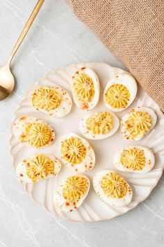 deviled eggs are arranged on a white plate with gold spoons next to it