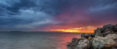 the sun is setting over the ocean with rocks in the foreground and clouds in the background