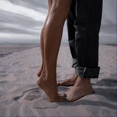 two people standing in the sand with their bare feet on top of each other's legs