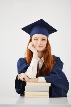 Dreamy graduate woman smiling thinking sitting with books over white surface Free Photo Successful Student Photo, Education Graduate Pictures, Graduation Photoshoot With Books, Graduate Studio Photoshoot, Grad Photos With Books, Graduation Shoot Studio, Graduation Photos Studio, Studio Graduation Photos, Graduation Photoshoot Indoor