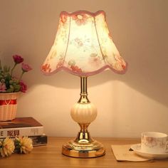 a lamp on a table next to a cup and saucer with flowers in it