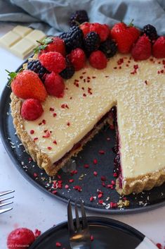 a cheesecake with berries and raspberries on top sits on a black plate