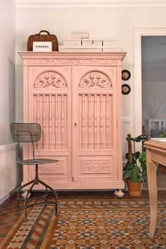 a pink armoire sitting in the corner of a room next to a desk and chair