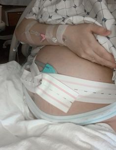 a pregnant woman in a hospital bed with her arm wrapped around the belly and attached to an iv tube