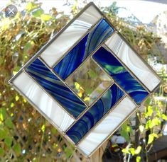 a blue and white square shaped glass piece hanging from a tree branch with leaves in the background