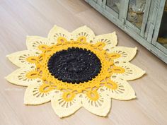 a yellow and black crochet doily sitting on the floor next to a cabinet