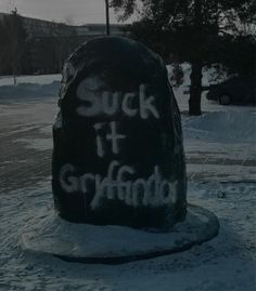 a large rock with writing on it in the middle of snow covered ground next to trees