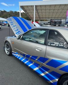 a silver car with blue stripes and a surfboard on it's hood is parked in a parking lot