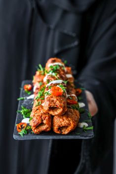 a person holding a tray with some food on it and garnished with herbs