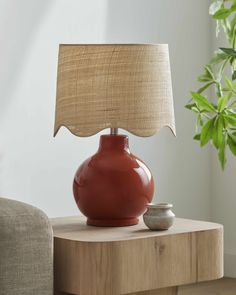 a table lamp sitting on top of a wooden table next to a chair and potted plant