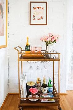 a bar cart with wine glasses, champagne bottles and flowers on the top is shown