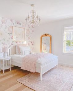 a white bed sitting in a bedroom next to a window with a chandelier