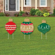 three christmas ornaments sitting on top of grass in front of a house