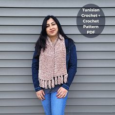 a woman standing in front of a gray wall wearing a tan scarf and blue jeans