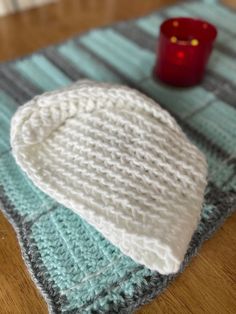 a white knitted hat sitting on top of a table next to a red candle