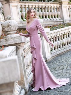 a woman in a long dress leaning against a wall with her hands on the railing