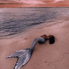 a woman laying on top of a sandy beach next to the ocean under a pink sky