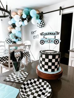 a black and white cake sitting on top of a table next to a balloon filled wall