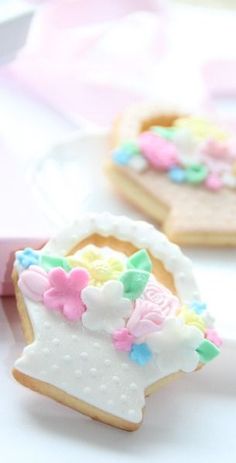 two decorated cookies sitting on top of a white plate next to a pink box with flowers