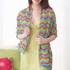 a woman standing in front of a couch wearing a crocheted cardigan