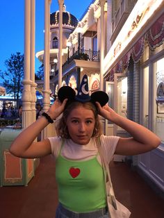 a girl is holding her ears up in front of the camera while wearing mickey mouse ears