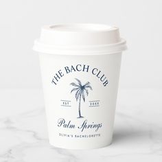 a white coffee cup sitting on top of a marble counter topped with a palm tree