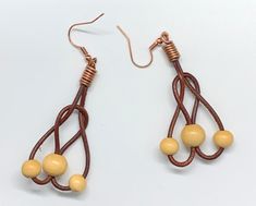 a pair of earrings with yellow beads hanging from brown cords on a white table top