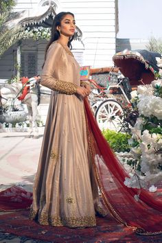 a woman in a long dress standing on a rug with flowers and a horse drawn carriage behind her