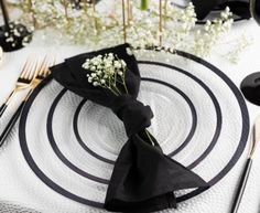 a place setting with black napkins, silverware and baby's breath flowers