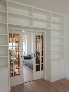 an empty living room with white bookcases and wood flooring is seen through the glass doors