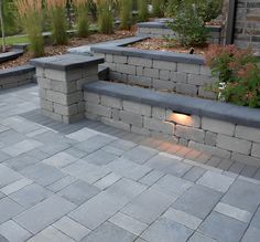 a stone bench sitting on top of a patio next to a brick wall and planter