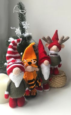 three crocheted gnomes next to a small christmas tree with a lit candle