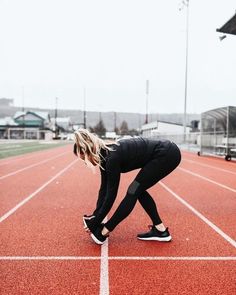 a woman kneeling down on top of a red running track with her hands in her pockets