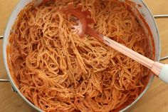 a pot filled with noodles and sauce on top of a wooden table