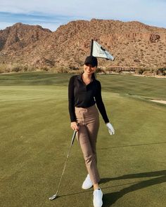 a woman walking across a green holding a golf club