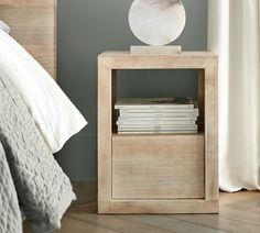 a nightstand with books on top of it next to a bed