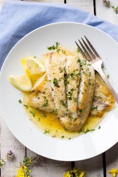 a white plate topped with chicken covered in lemon sauce and garnished with parsley