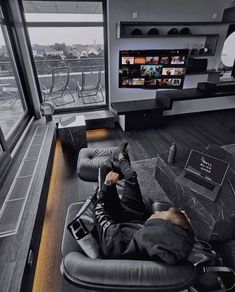 a man laying on top of a black leather chair in front of a large window