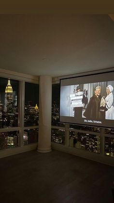 an empty room with a large screen on the wall and city lights in the background