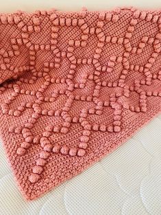 a pink crocheted blanket laying on top of a bed