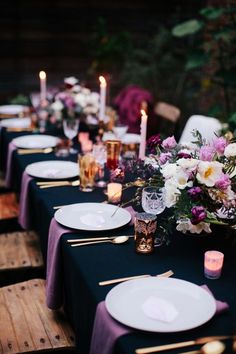 the table is set with purple and white flowers, candles, and place settings for dinner