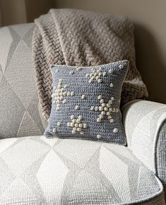 a crocheted pillow sitting on top of a couch next to a gray blanket